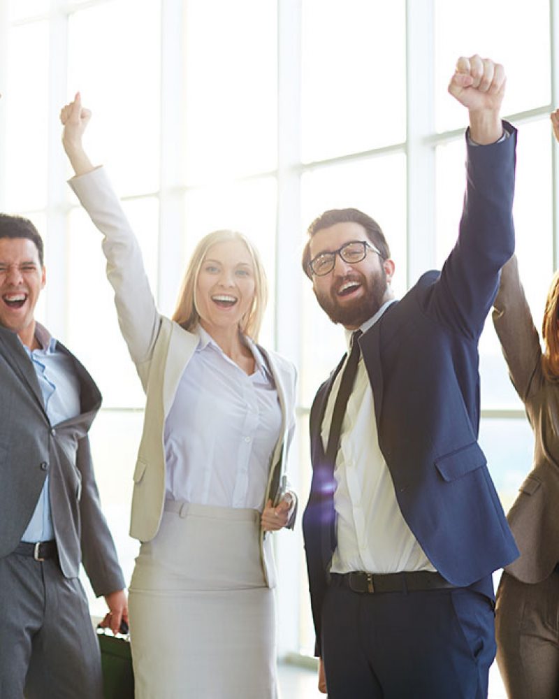 Group of ecstatic business partners looking at camera with raised arms